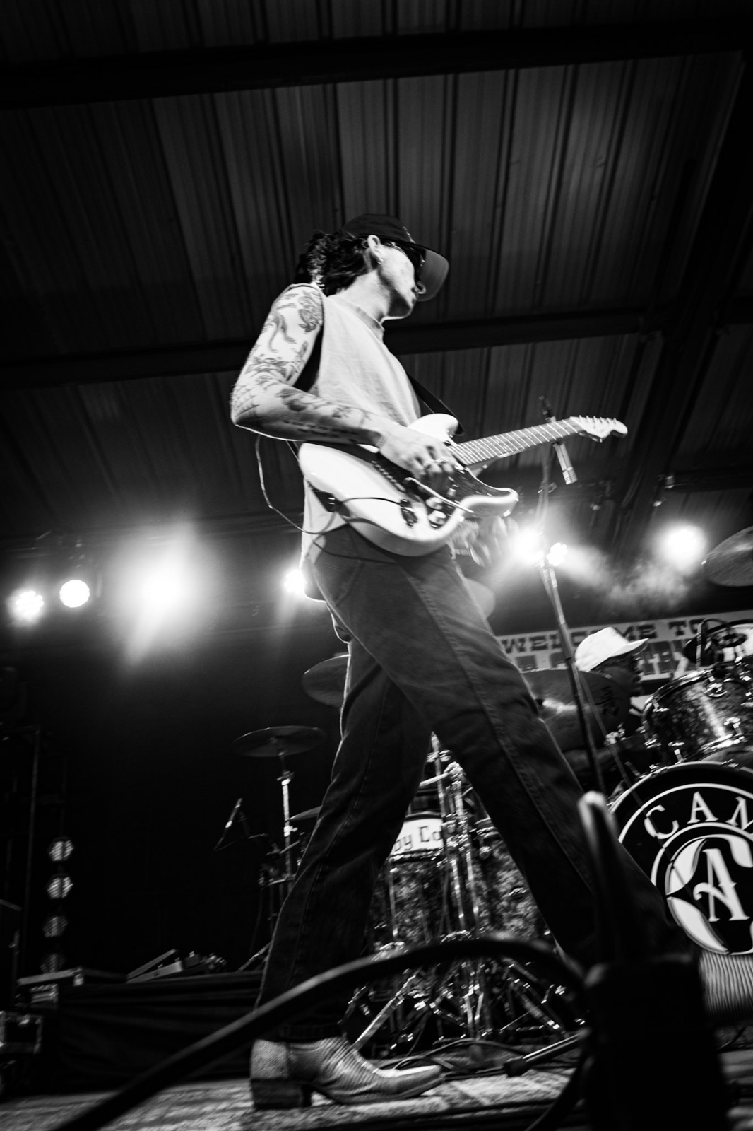 Black-and-white shot of Zander playing electric guitar on stage in cowboy boots