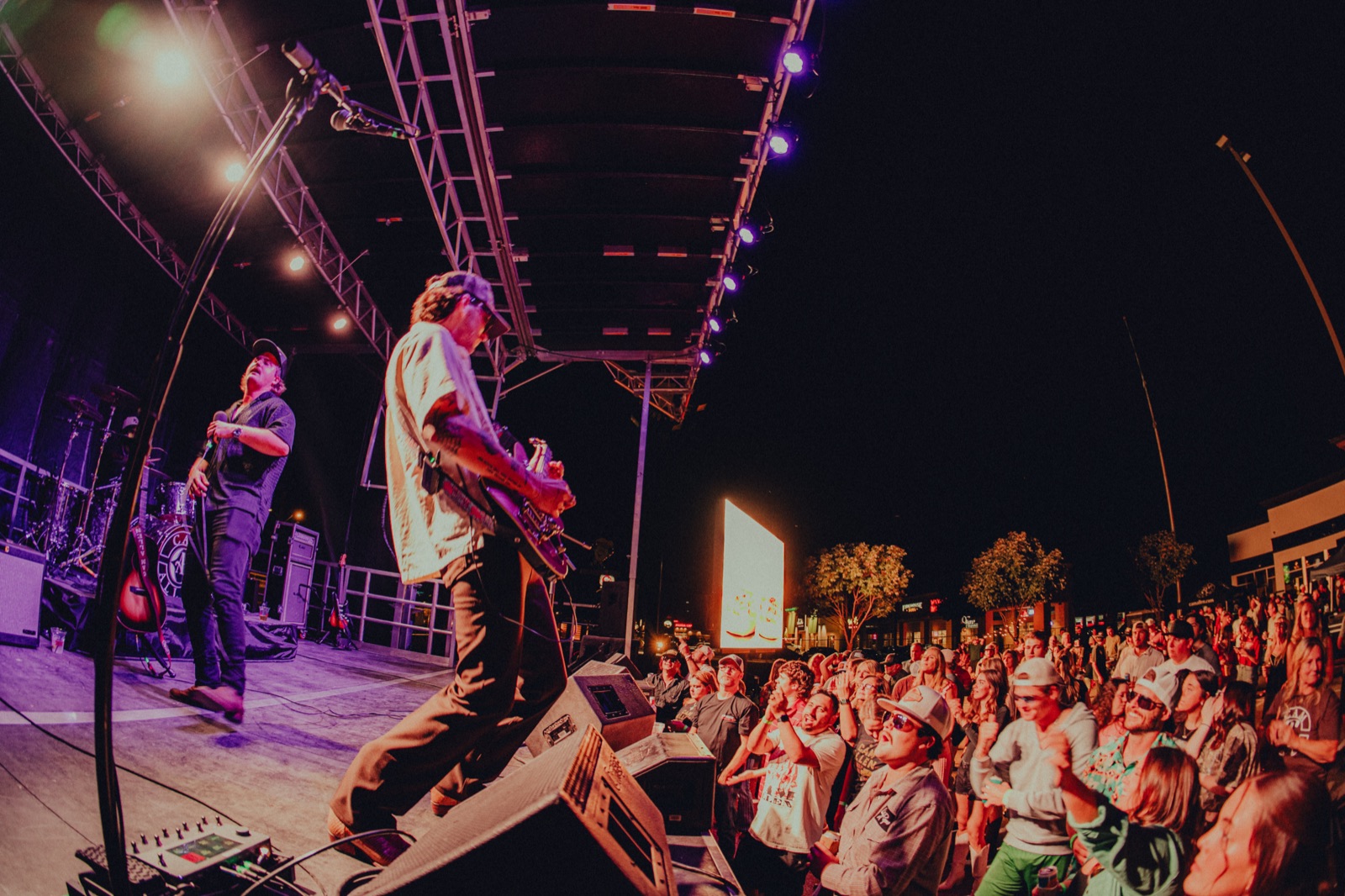 Playing guitar at an outdoor stage in front of a packed evening crowd