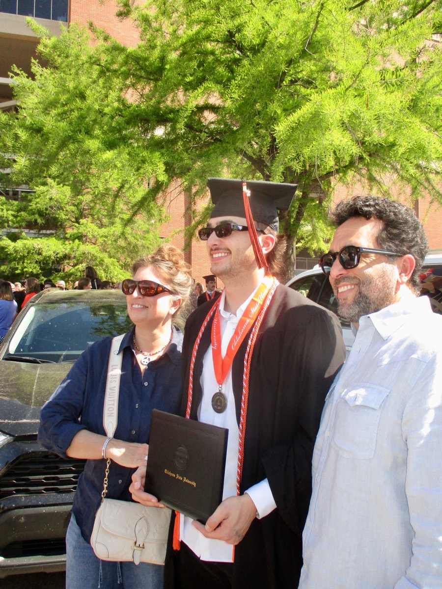 Zander in cap and gown at Oklahoma State graduation, holding his diploma with his parents